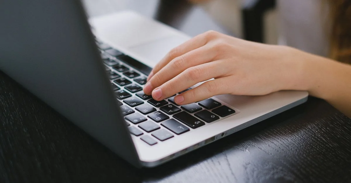 Gros plan d'une main tapant sur le clavier d'un ordinateur portable placé sur un bureau en bois.