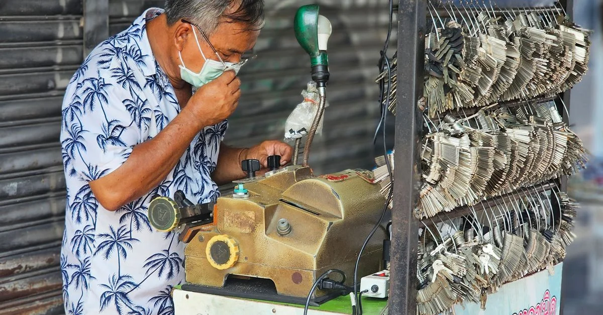 Un serrurier asiatique utilise une machine à clés mobile à l'extérieur. Scène commerciale du matériel informatique.