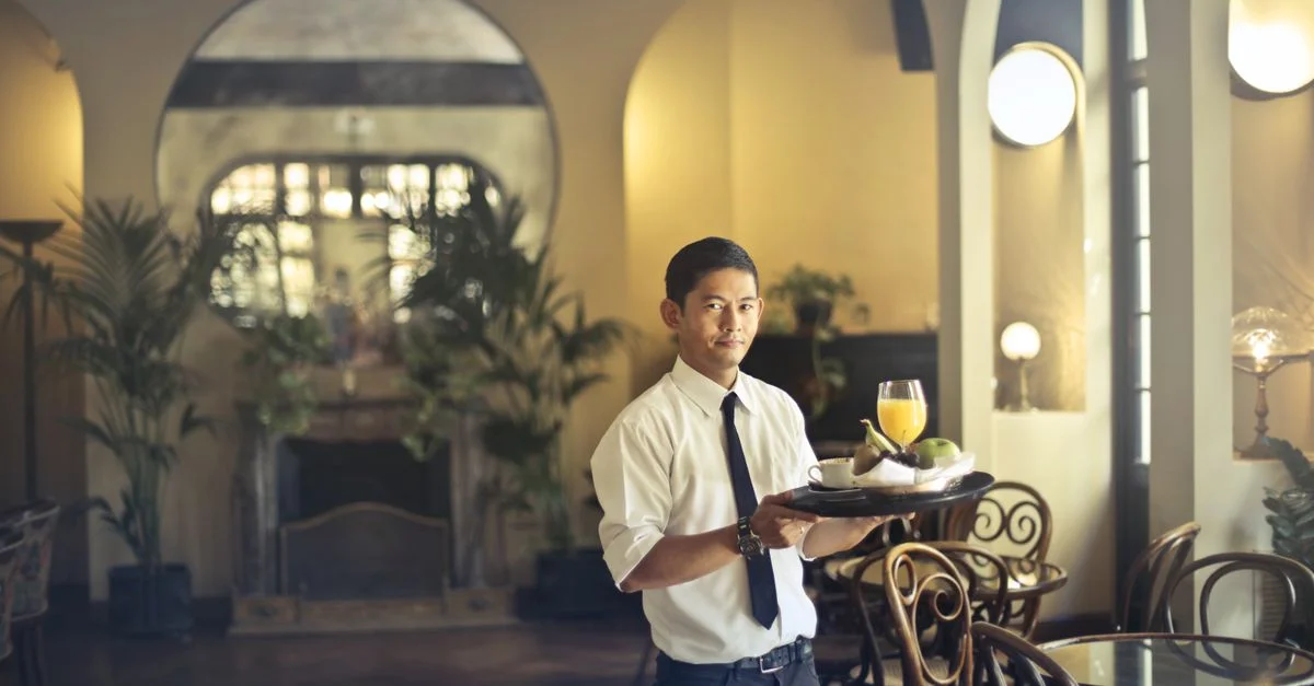 Serveur professionnel servant des boissons dans un élégant restaurant de style vintage avec un éclairage tamisé.