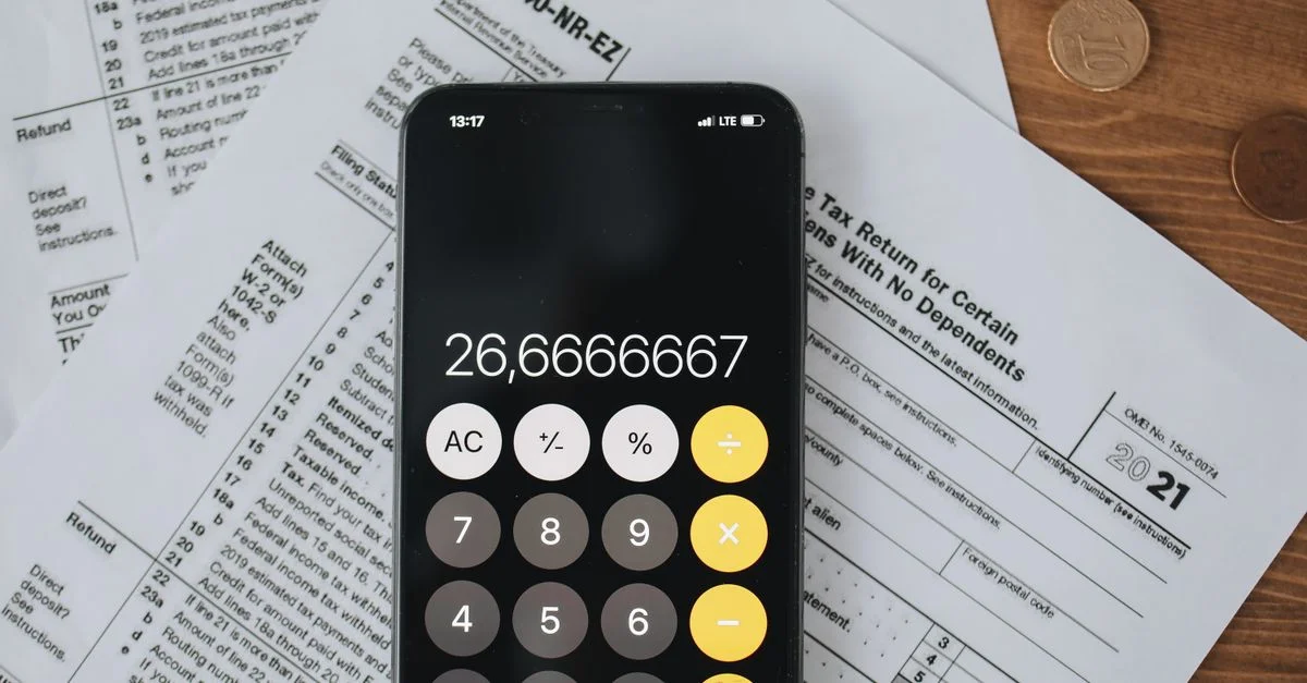 Calculatrice sur smartphone sur des formulaires fiscaux avec des pièces de monnaie, symbolisant le calcul des impôts et les finances.