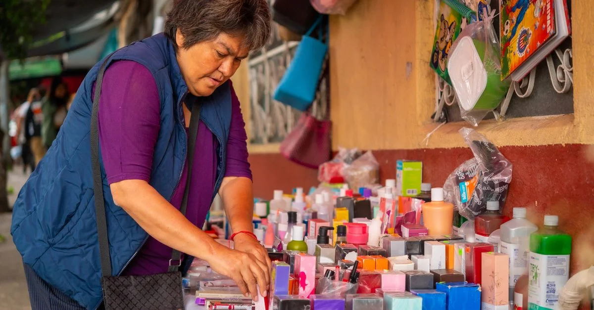 Une femme arrange des cosmétiques colorés à un stand de marché extérieur, promouvant la culture du shopping local.