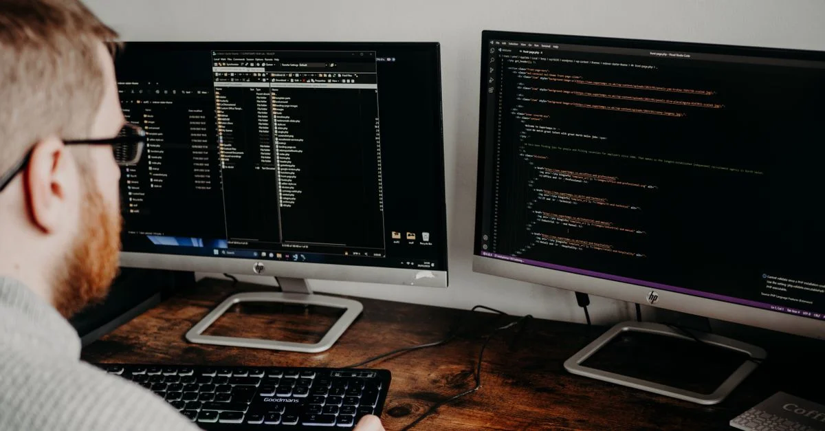 Développeur de logiciels travaillant sur du code avec des écrans doubles dans un bureau à domicile.