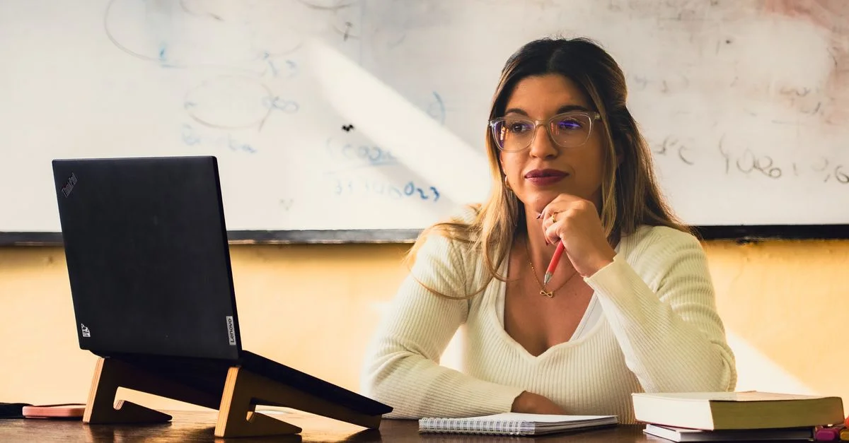 Jeune femme dans un bureau, travaillant sur un ordinateur portable, l'air pensif, avec des livres et des notes.
