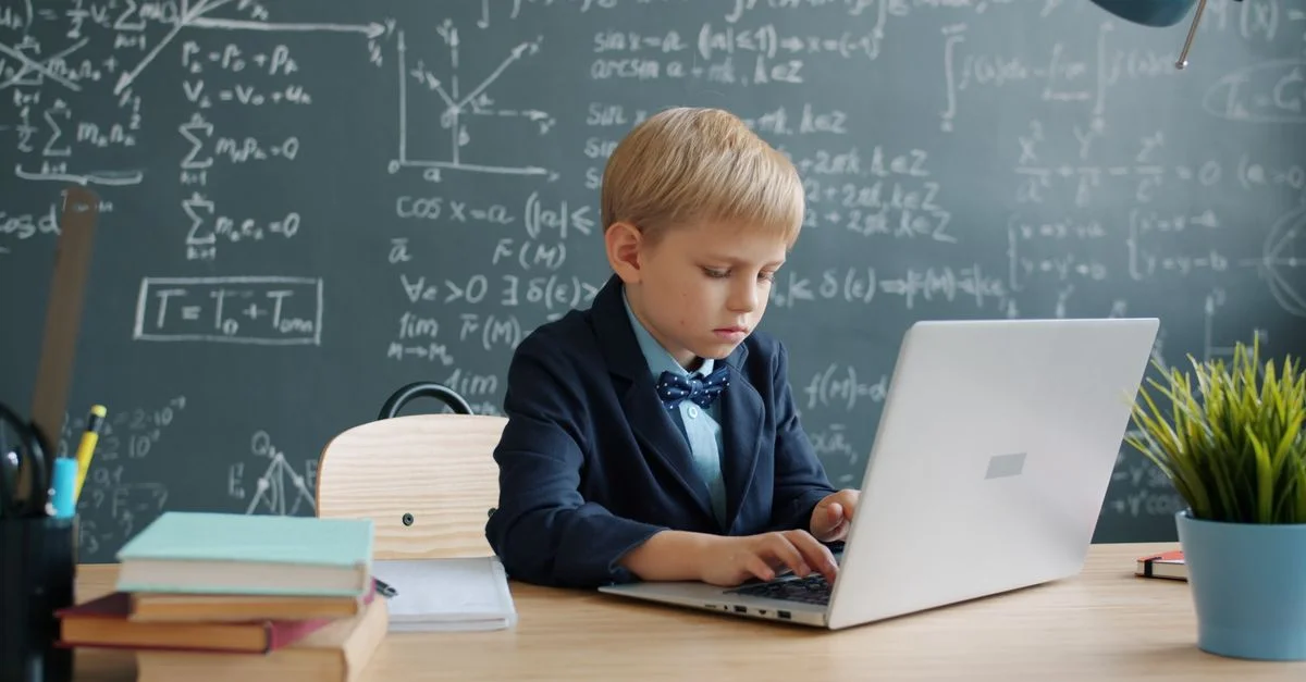 Un jeune garçon en costume utilise un ordinateur portable dans une salle de classe.