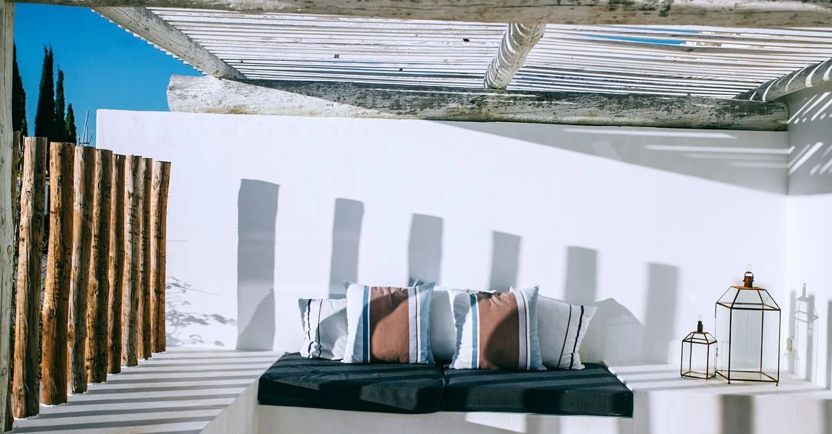 Terrasse extérieure relaxante avec des coussins élégants sous une pergola en bois au soleil éclatant.