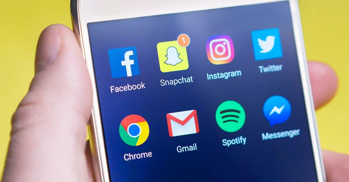 Une main tenant un smartphone affichant des applications de réseaux sociaux et de communication.