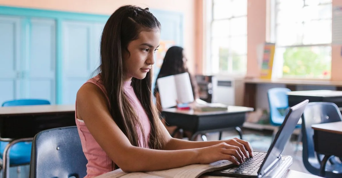 Jeune fille utilisant un ordinateur portable dans une salle de classe, illustrant un apprentissage concentré.