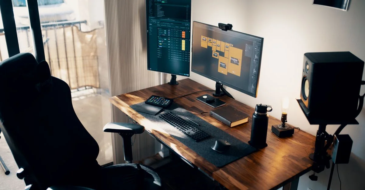 Configuration de bureau contemporaine avec des doubles écrans, une chaise ergonomique et un bureau en bois.