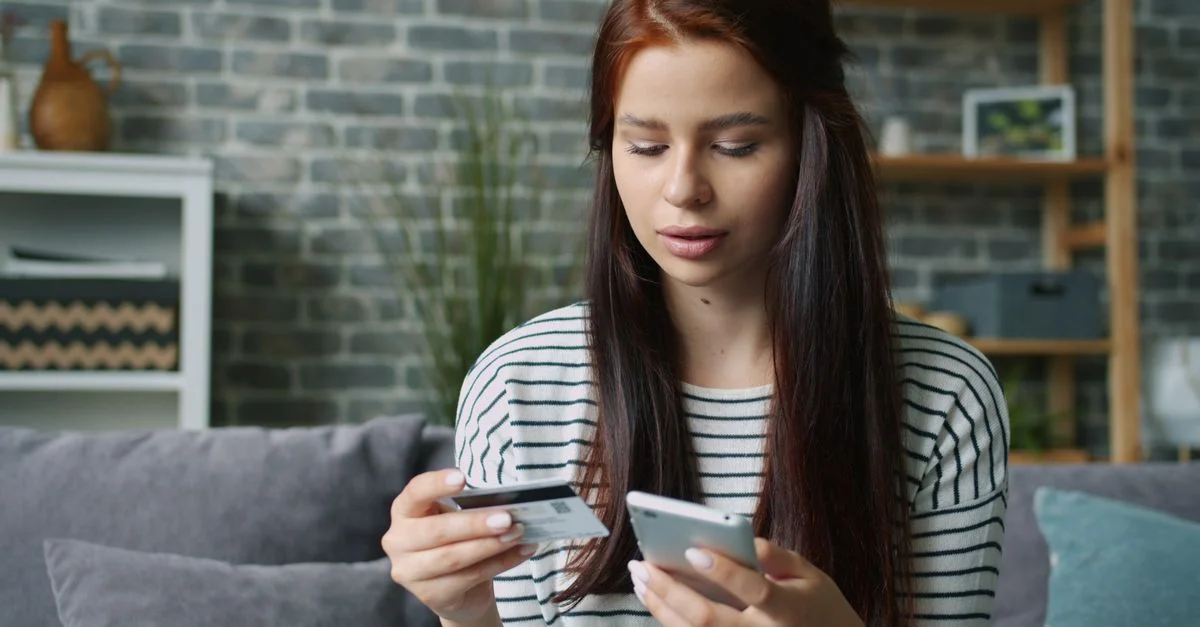 Femme utilisant un smartphone et une carte de crédit pour faire du shopping en ligne dans le salon.