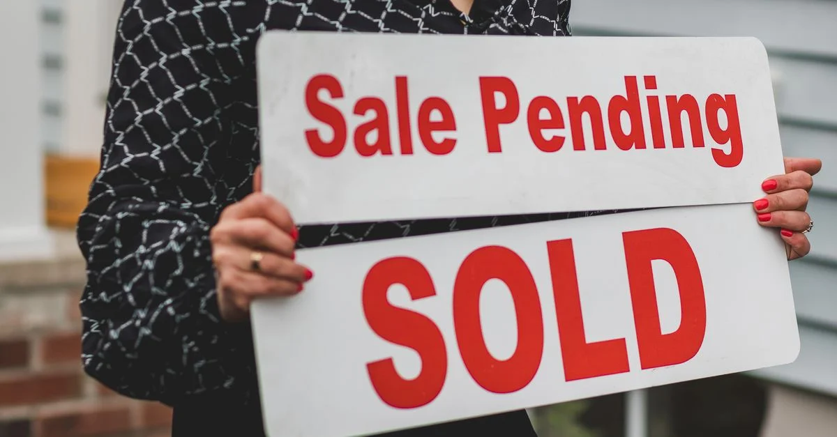 Une femme d'affaires tenant des panneaux 'Vente en cours' et 'Vendu' indiquant une transaction immobilière réussie.