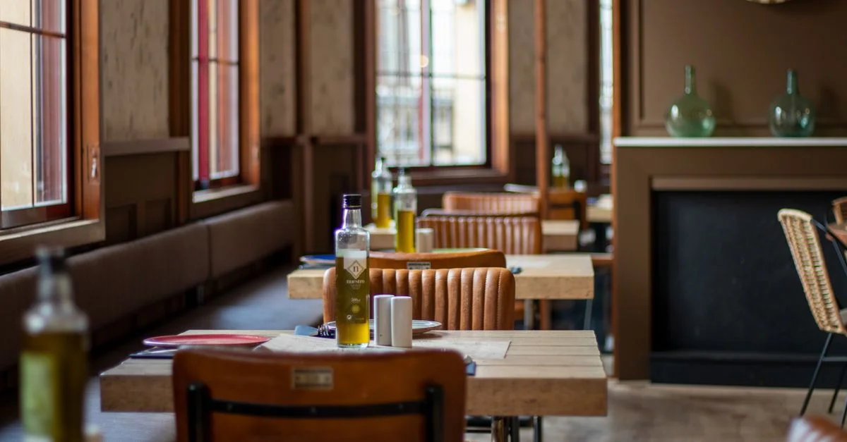 Intérieur de restaurant accueillant avec des tables en bois, des bouteilles d'huile d'olive et des chaises en cuir mises en valeur.