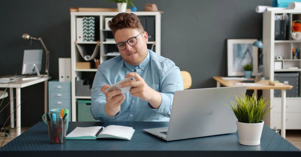 Homme souriant utilisant un smartphone à un bureau dans un bureau moderne.