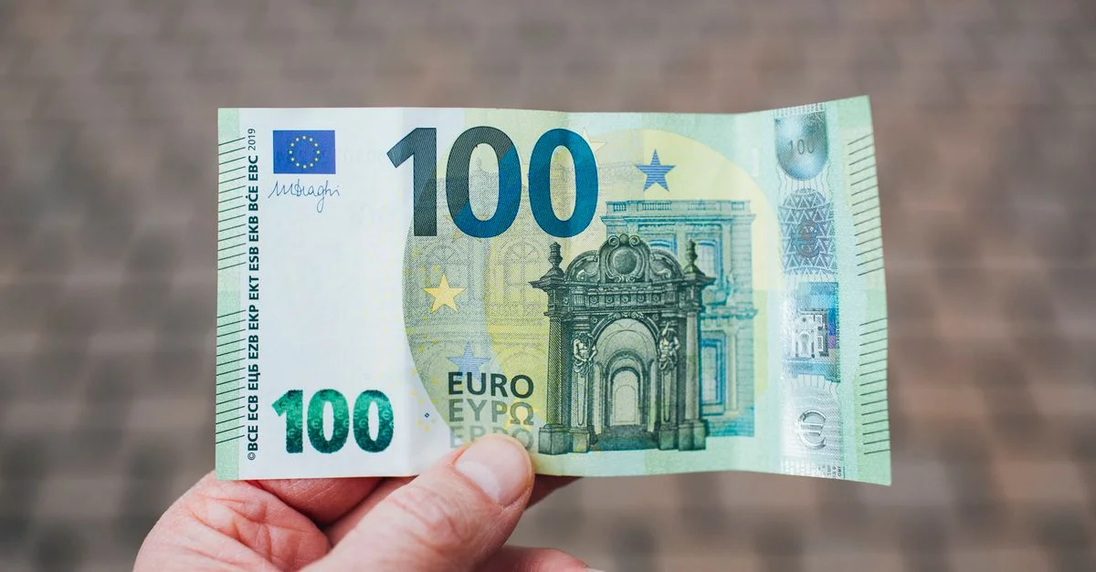 Photo en gros plan montrant une personne tenant un billet de 100 euros sur un fond flou.