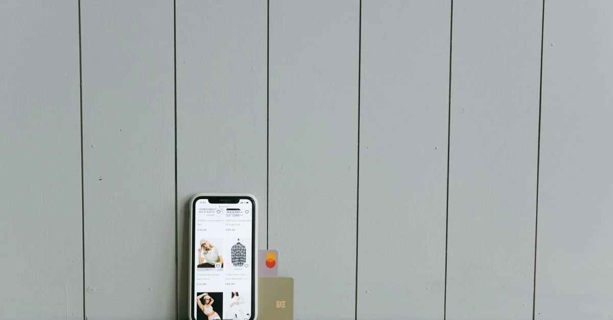 Un smartphone affichant un site e-commerce avec une carte de crédit, posé sur une surface en bois, illustrant le shopping en ligne.