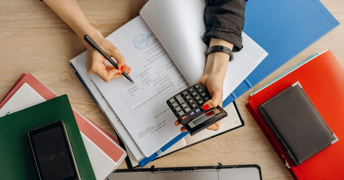 Comptable analysant des documents financiers avec une calculatrice sur un bureau, mettant en avant des tâches commerciales.