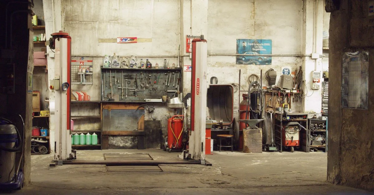 Un atelier automobile vide et rustique comprenant des outils, des machines et des élévateurs pour voitures dans un cadre industriel.