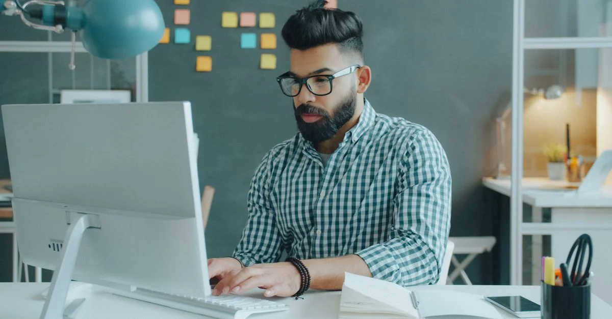 Jeune homme concentré sur son travail à son bureau, avec des post-it en arrière-plan.