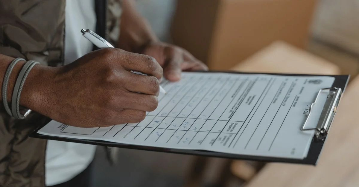 Gros plan sur une personne écrivant sur un formulaire attaché à un clipboard, capturant le processus diligent.