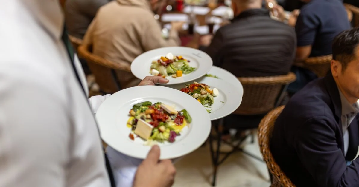 Un serveur sert des salades gastronomiques à un groupe de convives dans une ambiance de restaurant animée.
