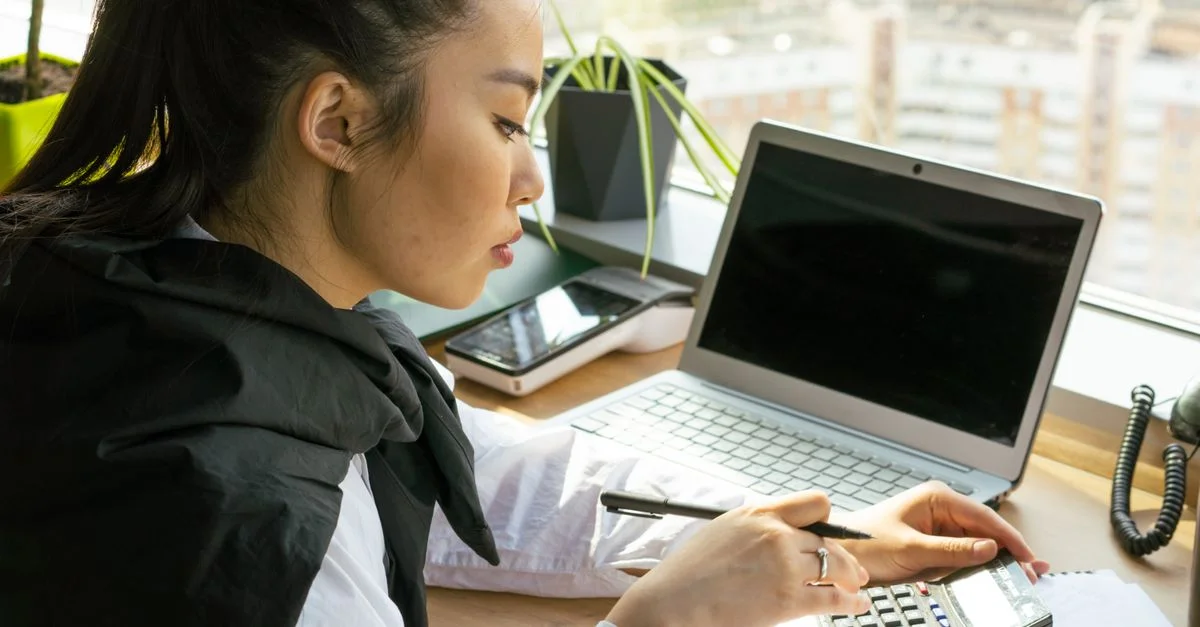 Femme asiatique travaillant dans un bureau lumineux, calculant des finances sur un bureau avec un ordinateur portable.