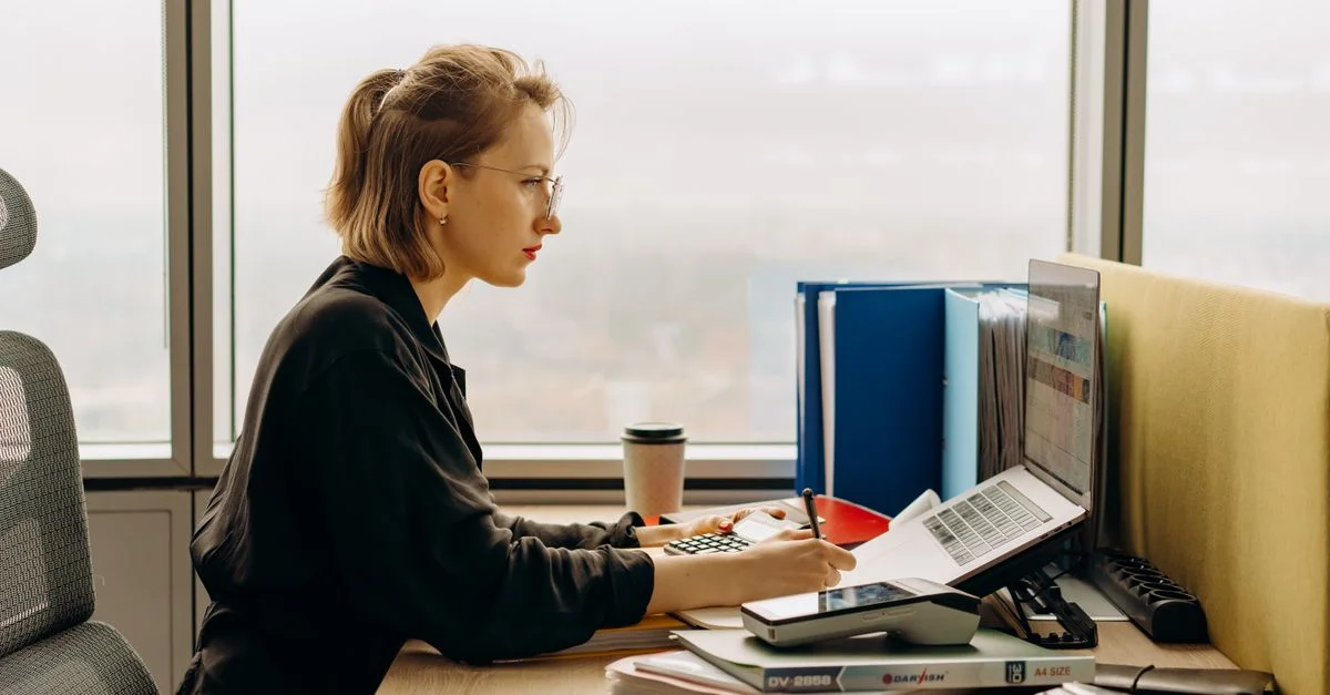 Femme dévouée utilisant un ordinateur portable et une calculatrice dans un bureau moderne.