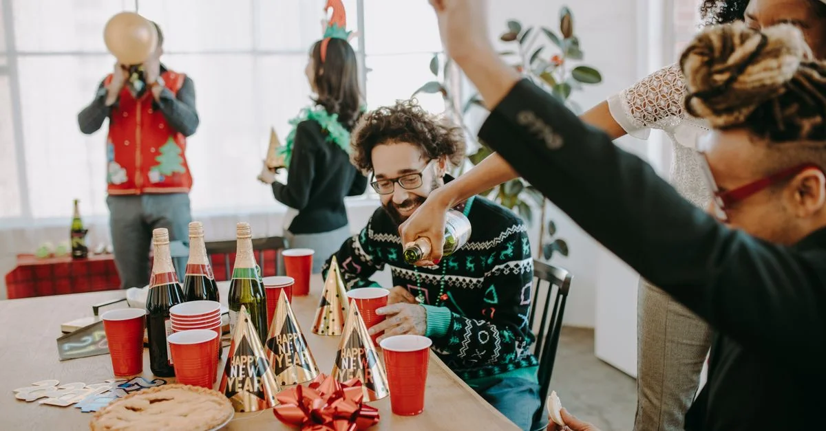 Des collègues profitent d'une fête festive du Nouvel An avec des boissons, des chapeaux et de la bonne humeur.