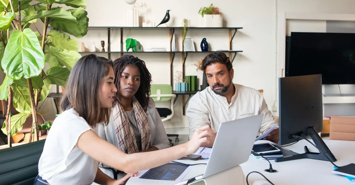 Un groupe diversifié de professionnels collaborant dans un environnement de bureau moderne, travaillant sur des ordinateurs portables autour d'une table.
