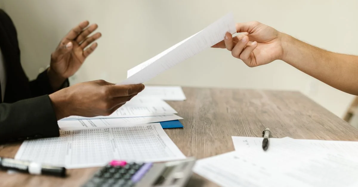 Deux professionnels échangeant des documents dans un cadre professionnel, mettant l'accent sur la collaboration et la paperasse.