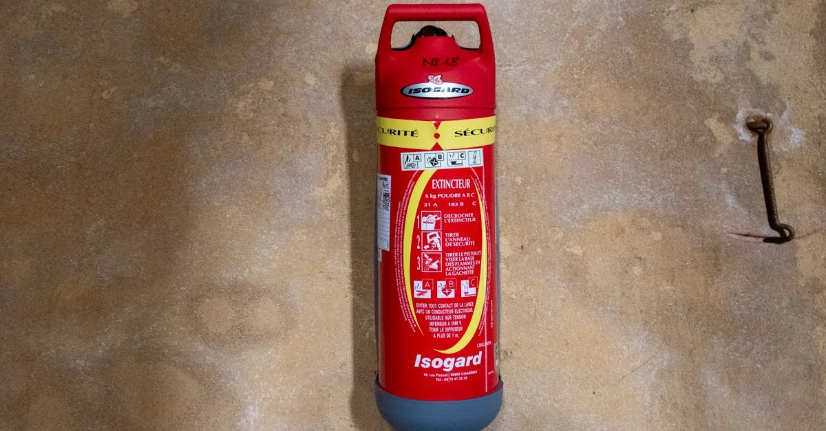 Extincteur Isogard rouge fixé sur un mur texturé, vue rapprochée.