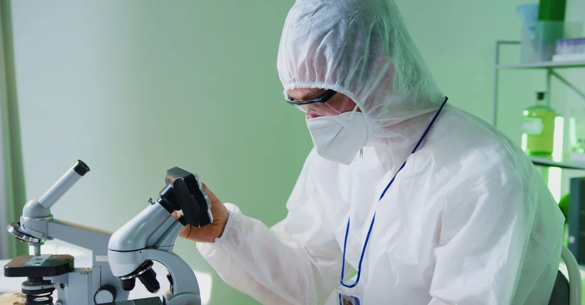 Un scientifique en équipement de protection examine des échantillons au microscope dans un laboratoire.