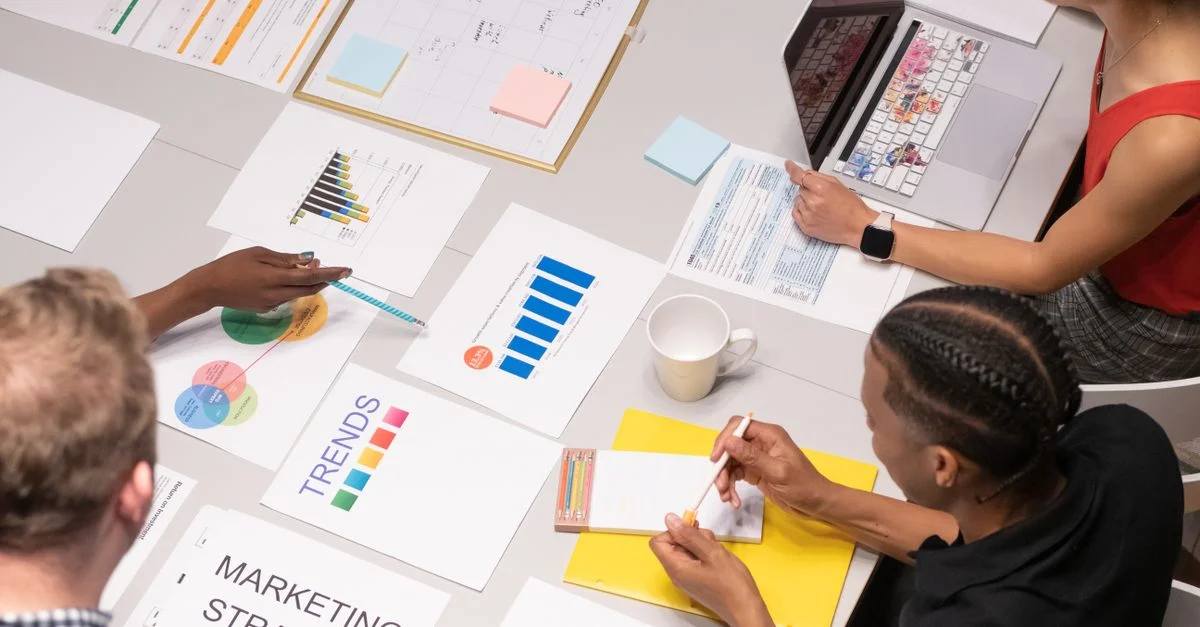 Prise de vue en plongée d'une équipe diverse analysant des stratégies marketing avec des graphiques et des tableaux.