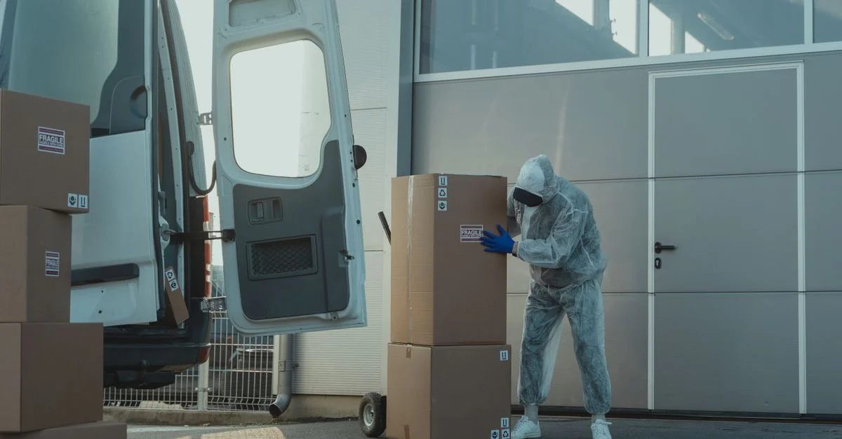 Un travailleur de livraison en EPI manipulant des cartons à l'extérieur d'un entrepôt avec une camionnette.