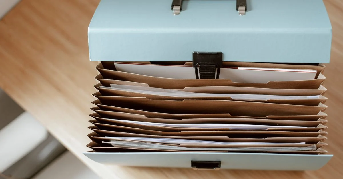 Une vue de dessus d'un dossier accordéon bleu rempli de documents de bureau organisés sur un bureau en bois.
