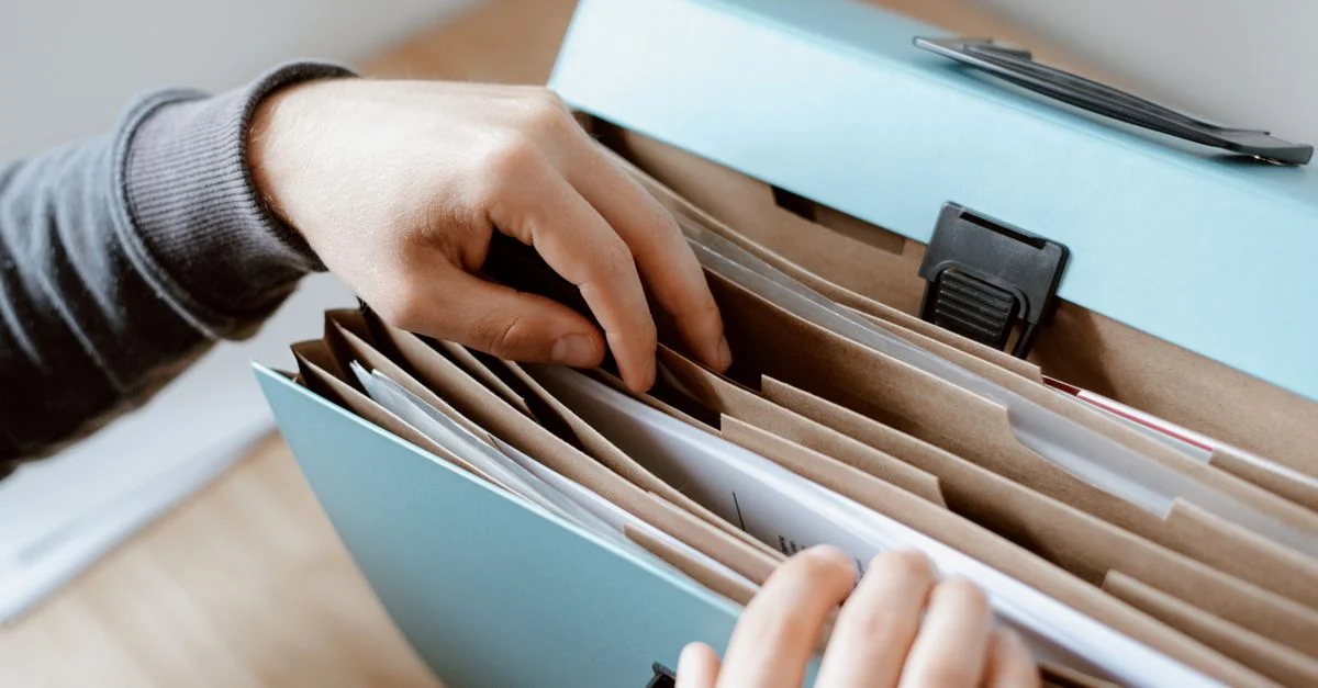 Gros plan sur des mains organisant des papiers dans un dossier bleu, idéal pour des concepts d'affaires et de bureau.