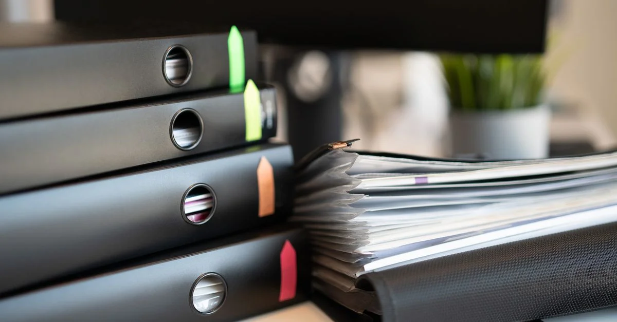 Pile de classeurs colorés et de documents sur un bureau de bureau moderne.