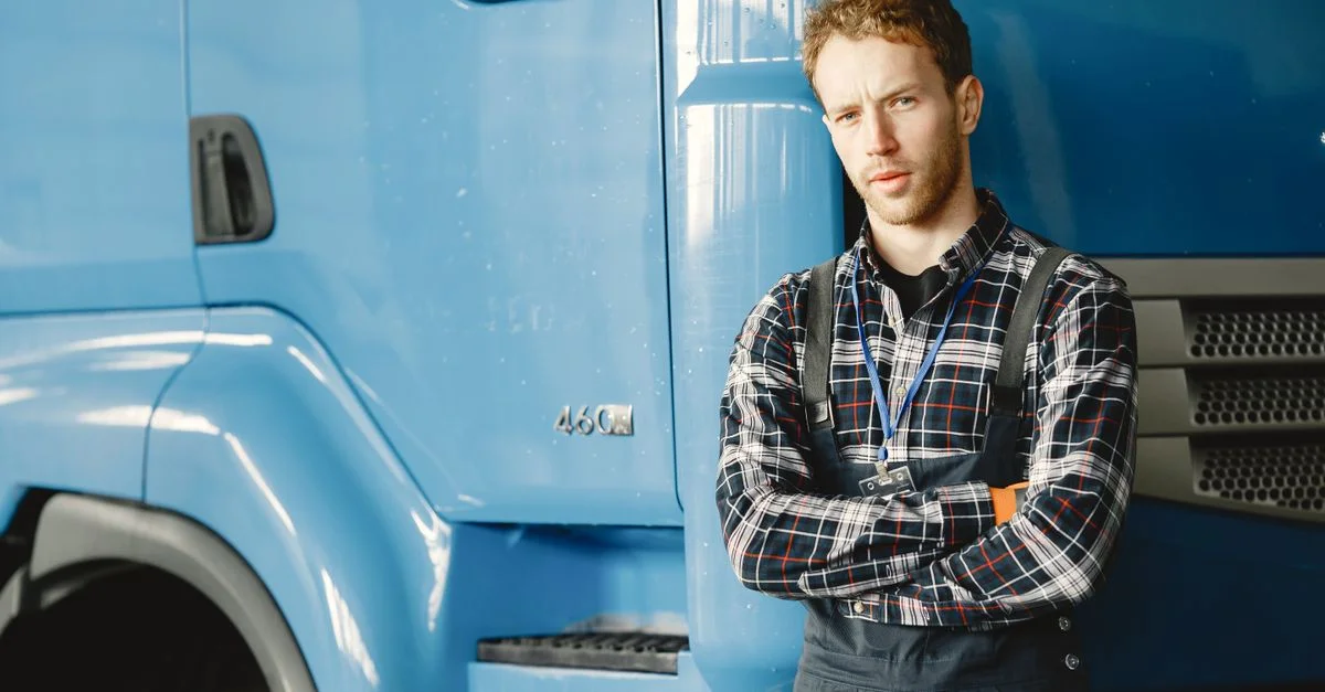 Mécanicien avec les bras croisés posant à côté d'un camion bleu dans un garage