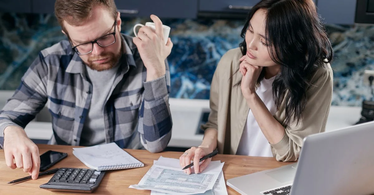 Un couple examine des factures et des documents sur un ordinateur portable tout en discutant des finances du ménage.