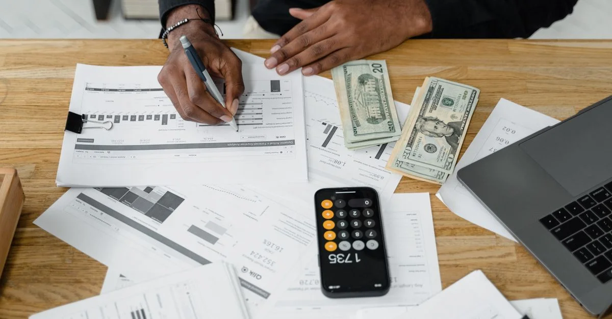 Homme travaillant sur des rapports financiers avec une calculatrice, de l'argent et un ordinateur portable sur un bureau.