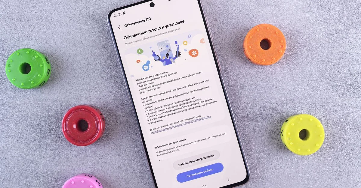 Plan rapproché d'un smartphone affichant une mise à jour du logiciel, entouré d'accessoires de jeu colorés sur un bureau gris.