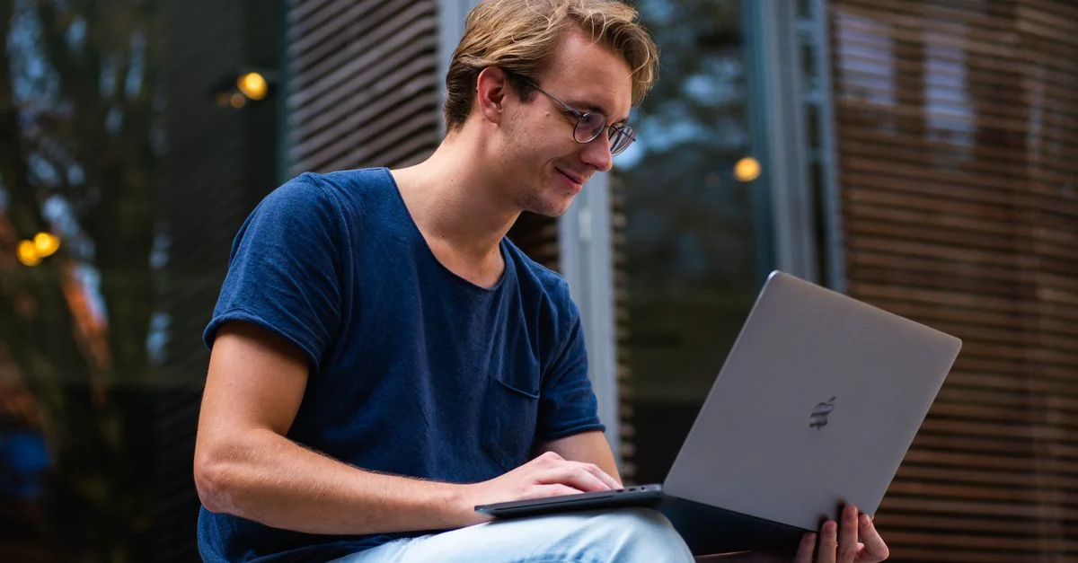 Un jeune homme assis à l'extérieur à Leiden, aux Pays-Bas, travaillant sur un ordinateur portable.