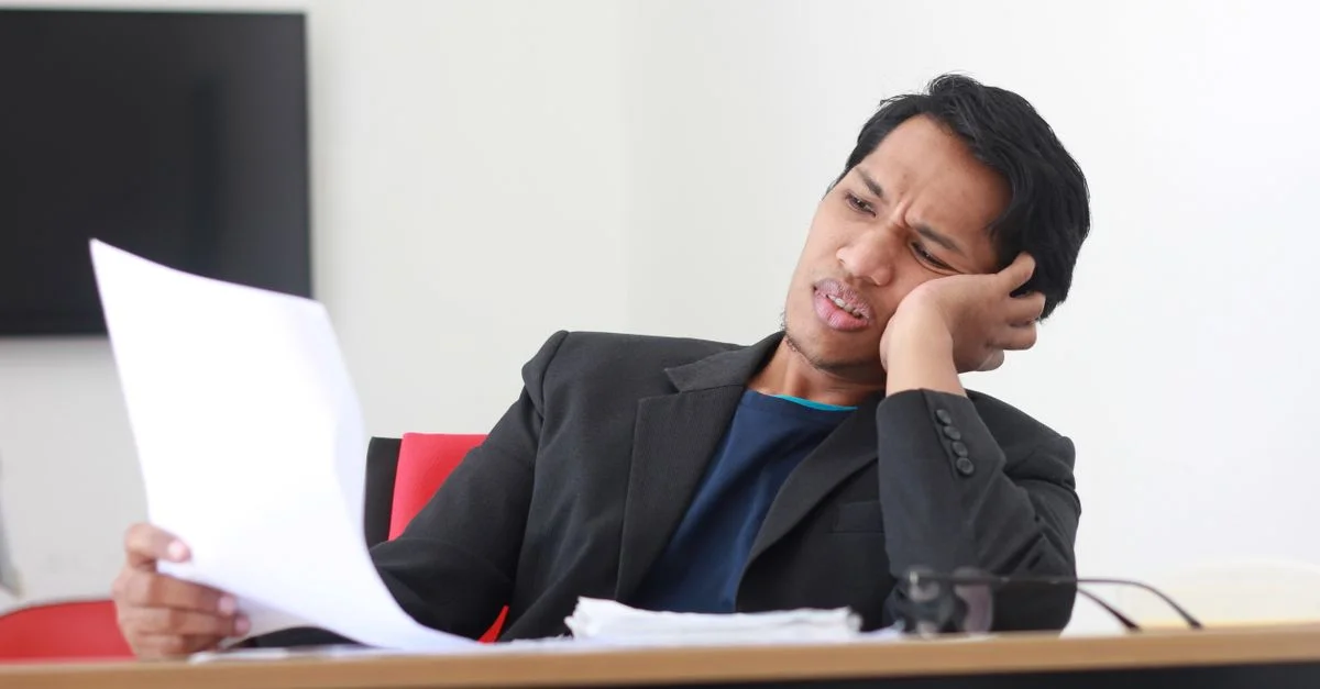 Un homme d'affaires en costume noir ressent du stress en examinant des documents dans un bureau moderne.