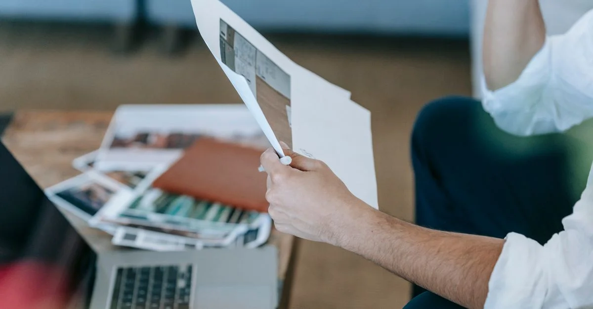Un homme assis sur un canapé, examinant des documents dans un espace de travail moderne avec un ordinateur portable.