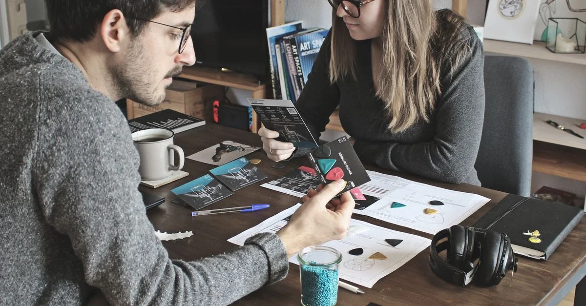 Deux adultes collaborant sur un projet de design à une table dans un salon moderne.