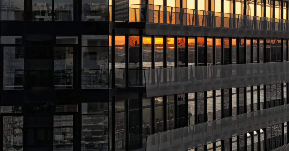 Façade d'immeuble urbain reflétant un magnifique coucher de soleil dans les fenêtres.