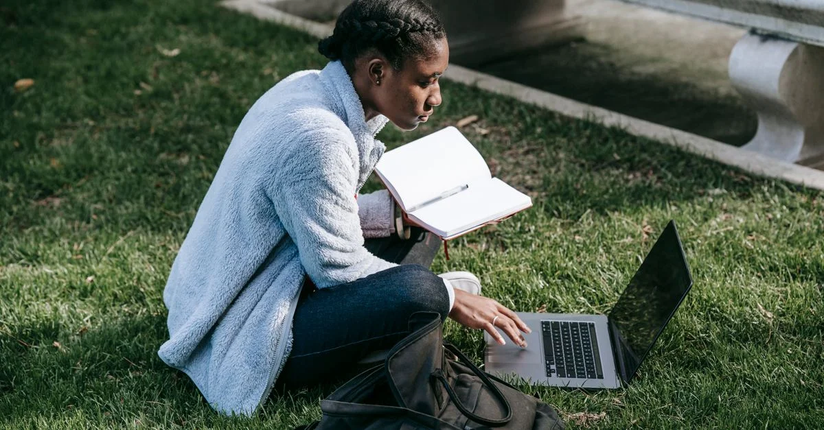 Jeune femme concentrée étudiant sur un ordinateur portable dans une pelouse de campus.