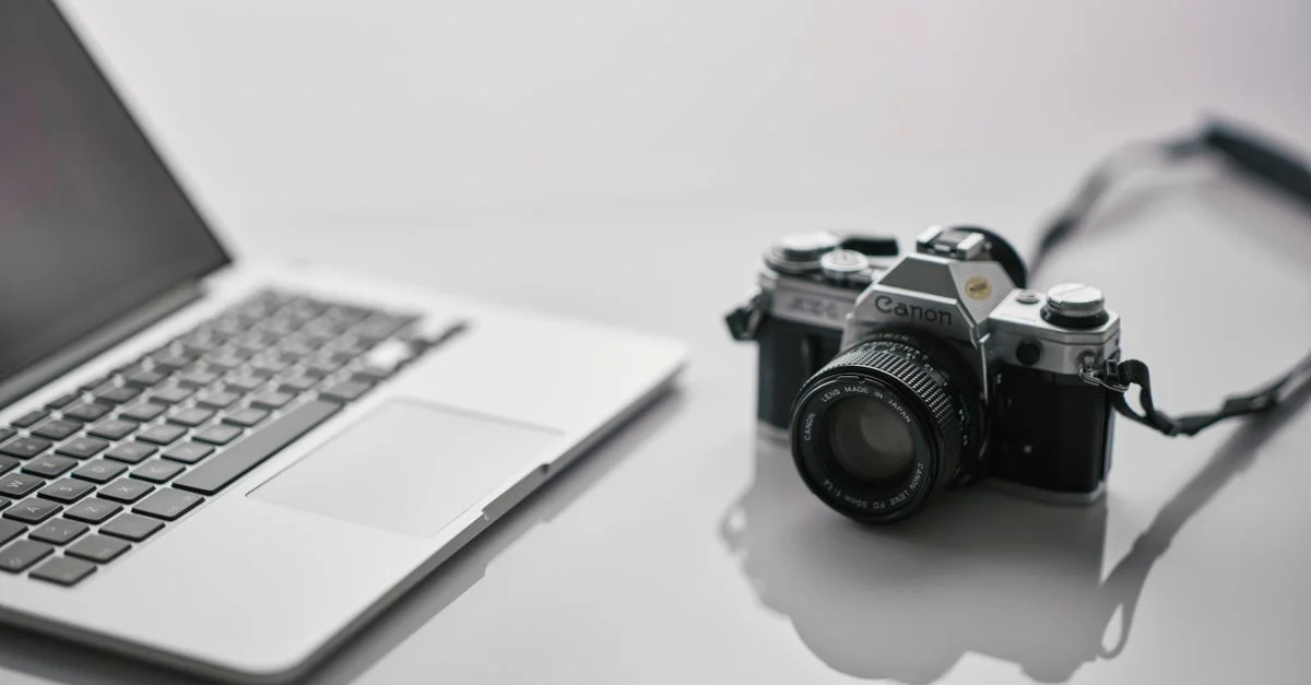 Un appareil photo Canon vintage et un ordinateur portable moderne sont disposés avec style sur un bureau réfléchissant.