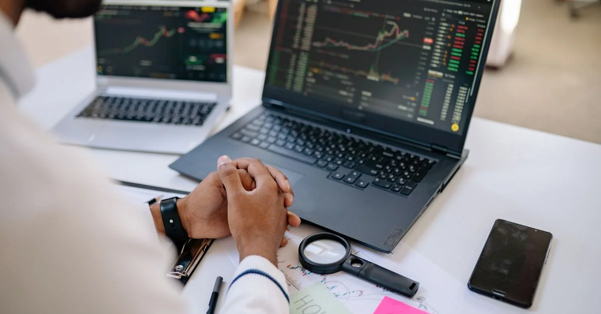 Professionnel du business analysant des données boursières sur des ordinateurs portables doubles dans un bureau.