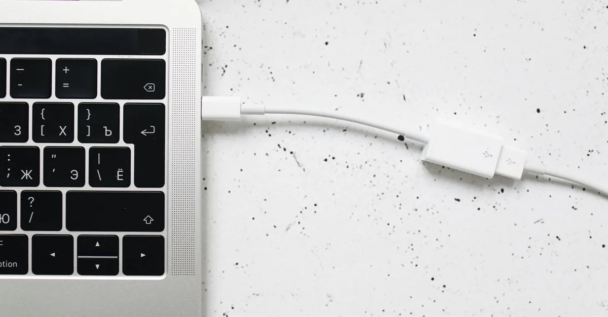 Gros plan sur un câble USB connecté au clavier d'un ordinateur portable sur une surface texturée blanche.