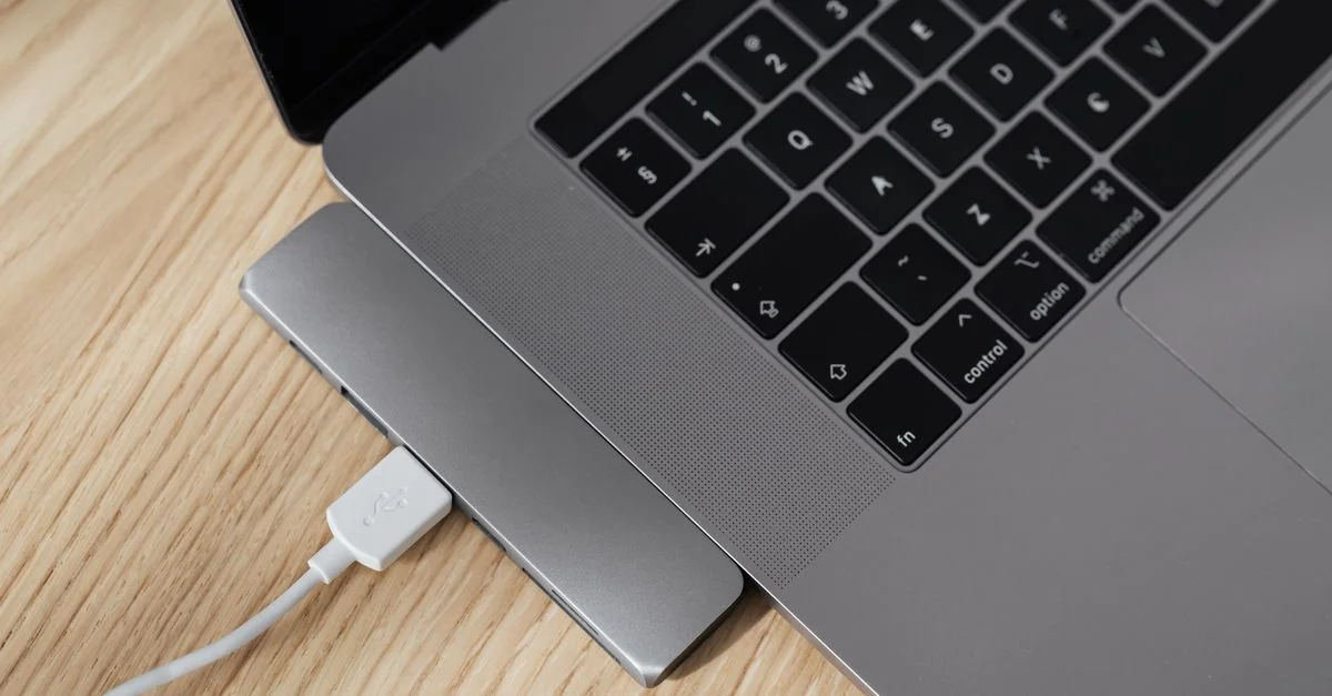 Gros plan sur un ordinateur portable avec un hub USB-C connecté sur un bureau en bois, capturant les détails de l'espace de travail.