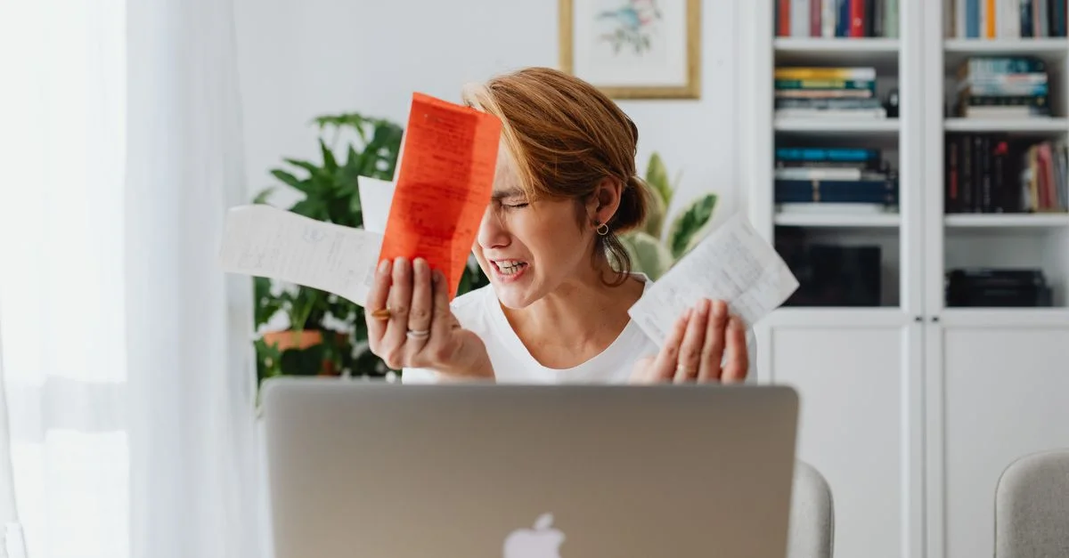 Femme frustrée gérant ses finances, entourée de factures et d'un ordinateur portable, ayant l'air préoccupée.